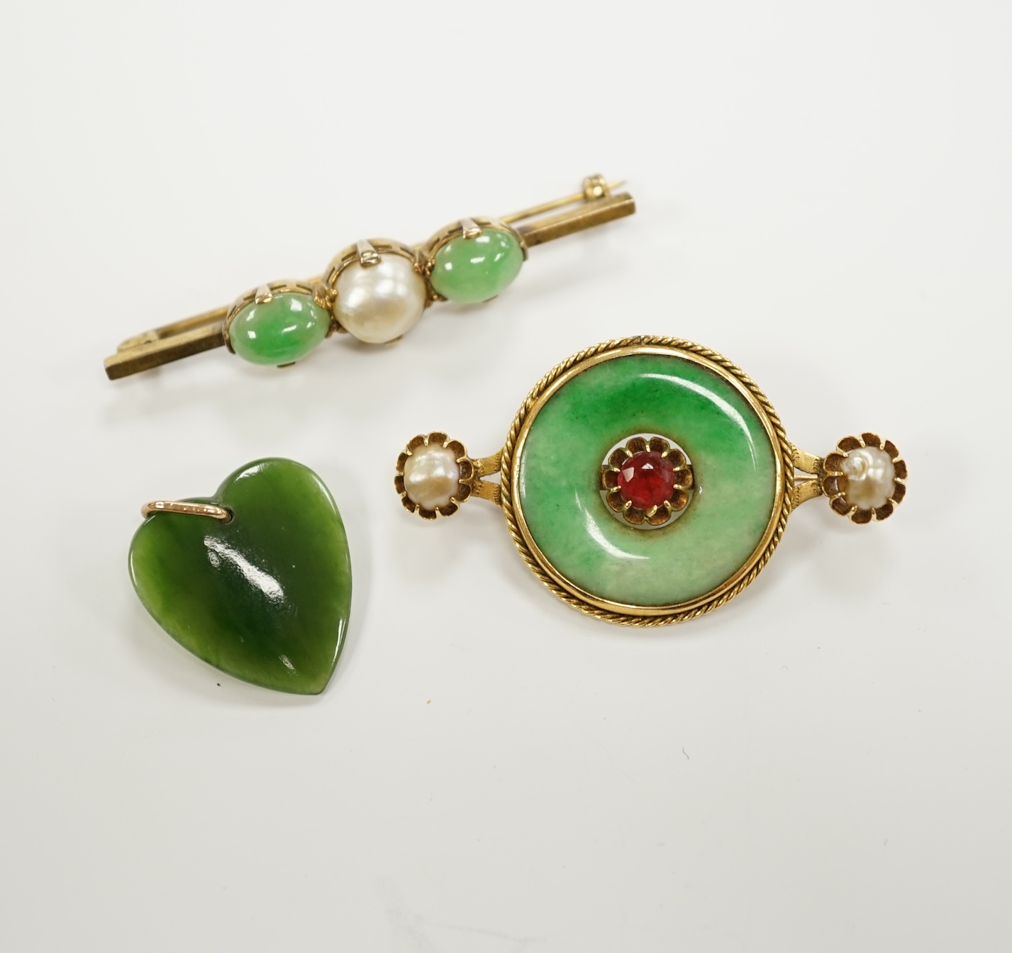 A Chinese 18k mounted, jade, cultured pearl and gem set disc brooch, 48mm, together with a yellow metal, jade and cultured pearl set bar brooch and a nephrite pendant.